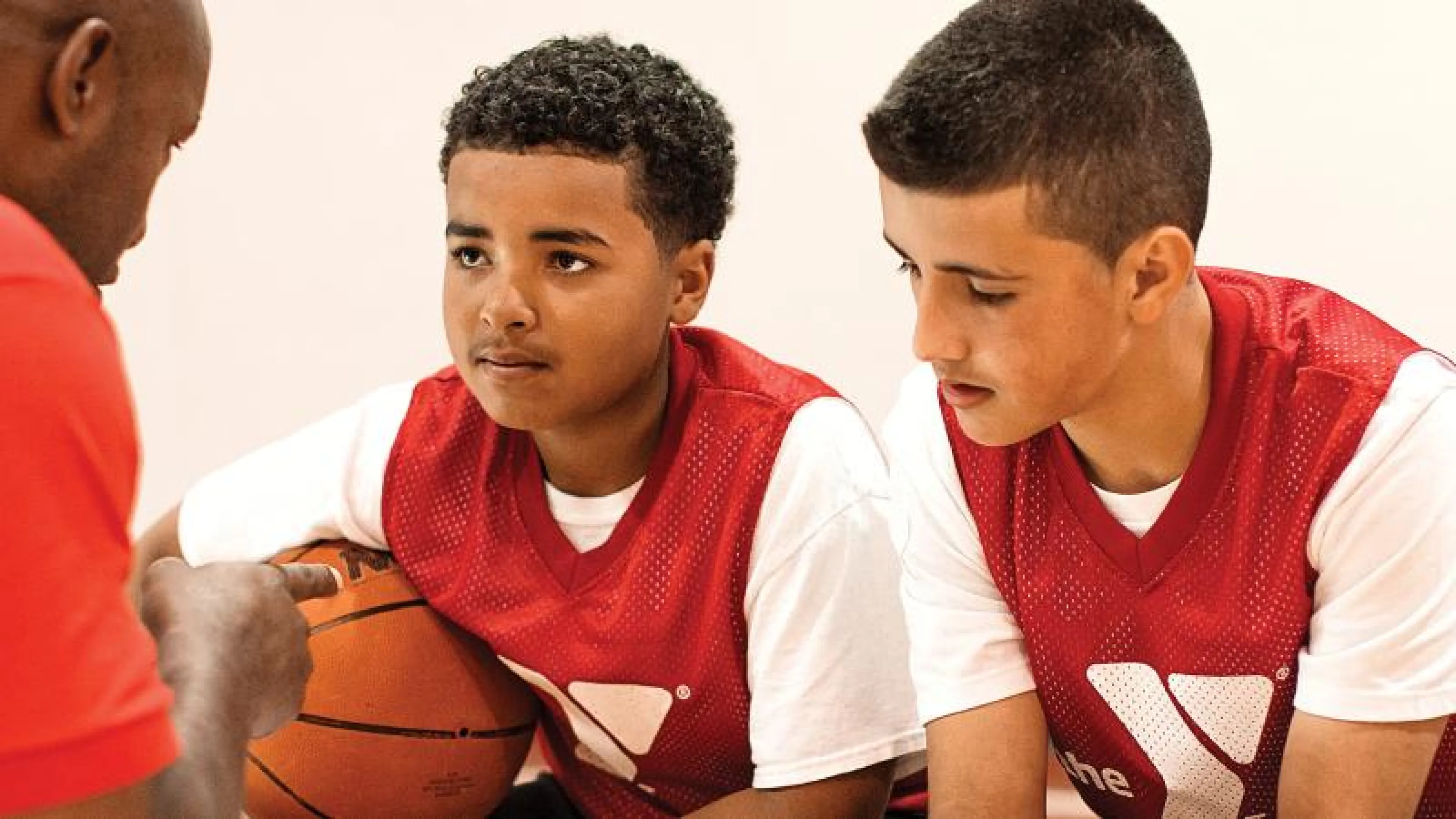 A coach instructing 3 youths in basketball.