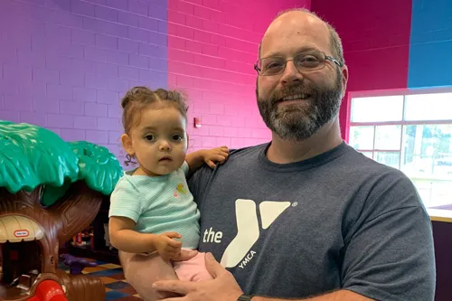 foster dad wearing YMCA shirt holding young daughter