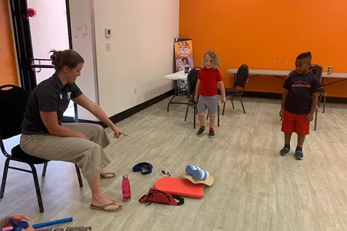 ymca staff pointing to swim flotation with children watching