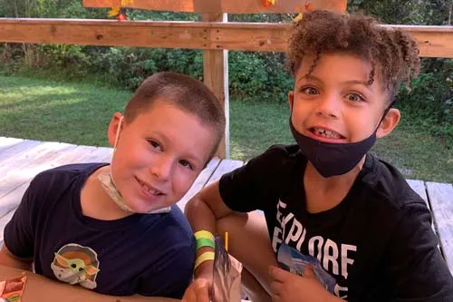 two kids smiling with masks at outdoor camp lunch table 