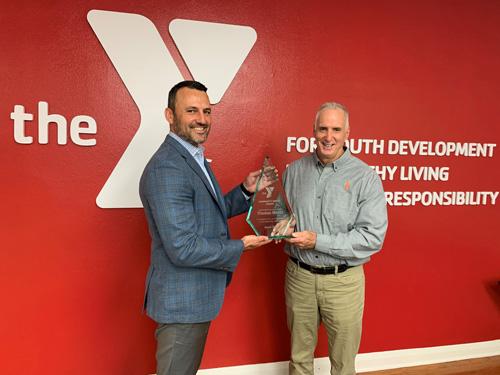 Tampa Y CEO Matt Mitchell presenting Feeding Tampa Bay CEO Thomas Mantz award in front of red wall with white YMCA logo