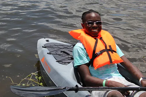 kid wearing sunglasses and lifejacket smiling and sitting in a kayak