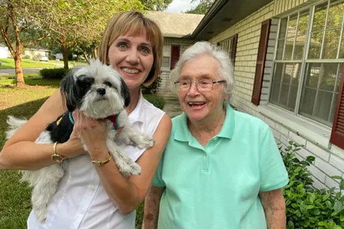 A woman holding a dog standing next to an elderly woman outside