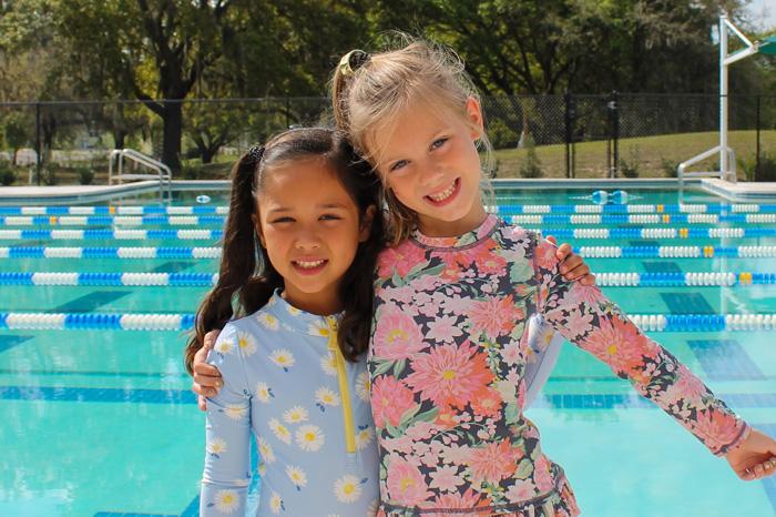 two swimmers on YMCA pool deck wearing rash guard bathing suits, smiling and hugging for a photo pose