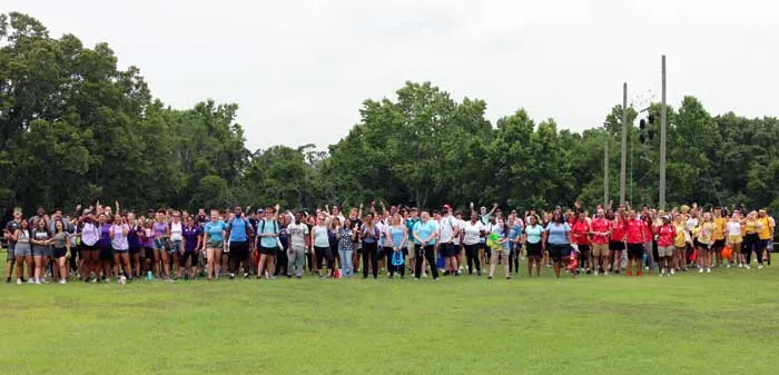 A few hundred Tampa Y summer camp counselors gather for a photo at YMCA Camp Cristina. The group is outdoors, on a field, each team wearing the same colors. 
