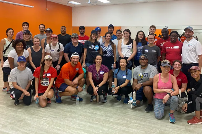 Indoor photo of 31 volunteers at the North Brandon Family YMCA. Background is an orange wall on the left, and white wall with exercise mirrors. 