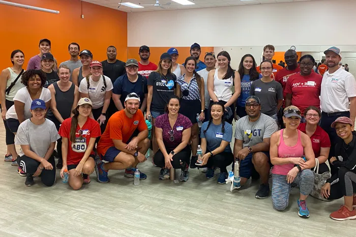 Indoor photo of 31 volunteers at the North Brandon Family YMCA. Background is an orange wall on the left, and white wall with exercise mirrors.