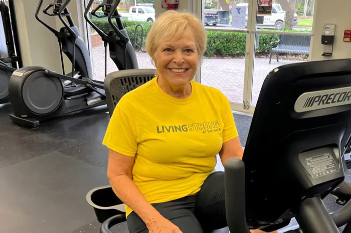 Woman wearing yellow shirt with "LIVESTRONG at the YMCA" sits at a recumbent bike.