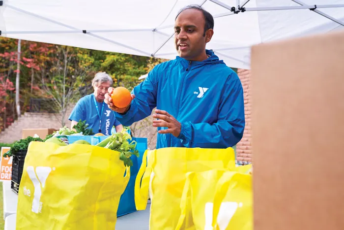Man sorting and food supplies from yellow grocery bags, preparing for distribution. Cardboard box in foreground.