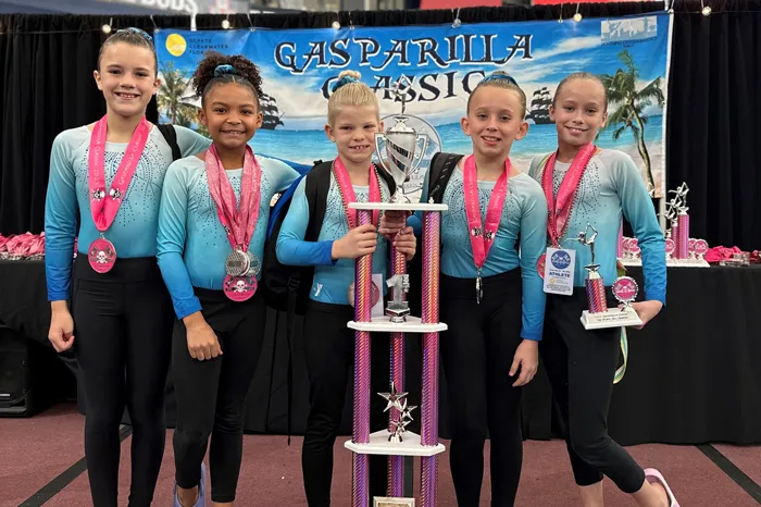 The 2023 Tampa Y Top Flight gymnastics team pose with their first place trophy at the Gasparilla Classic.