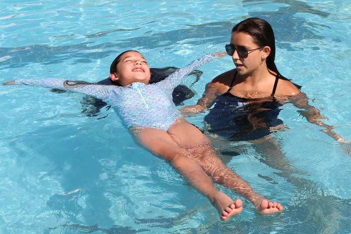 Swim instructor teaching a school age child how to float.