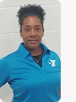 Female personal trainer wearing a blue YMCA Staff polo in front of a gray wall.