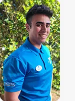 Male personal trainer wearing a blue YMCA polo in front of a green hedge
