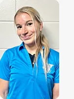 Female personal trainer wearing a blue YMCA Staff polo in front of a gray wall.