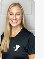 Female personal trainer wearing a black YMCA shirt in front of a gray wall.
