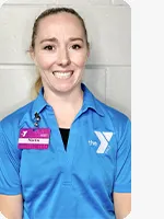Female personal trainer wearing a blue YMCA staff polo in front of a gray wall.