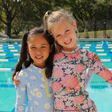 two swimmers on YMCA pool deck wearing rash guard bathing suits, smiling and hugging for a photo pose