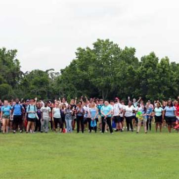 A few hundred Tampa Y summer camp counselors gather for a photo at YMCA Camp Cristina. The group is outdoors, on a field, each team wearing the same colors. 