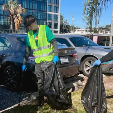 Two teens wearing yellow safety vests looking for trash in a parking lot during the MLK Day of Service 2023 cleanup.