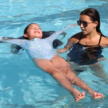 Swim instructor teaching a school age child how to float.