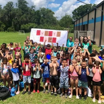A group of about 50 Plant City Y summer campers and counselors pose for an outdoor photo. Handmade banner in the background reads "Avery's Army" and features signatures from the group's campers.