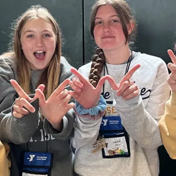 Four female teens wearing sweatshirts and making a W with their own hands pose with smiles.