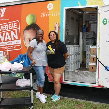 Two women in front of the Veggie Van with food in bags.